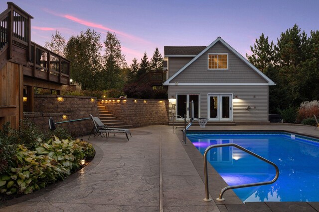 pool at dusk featuring a patio area, stairway, french doors, an exterior structure, and an outbuilding