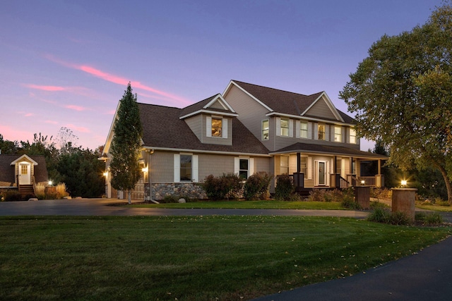 view of front facade with a porch, a lawn, and stone siding