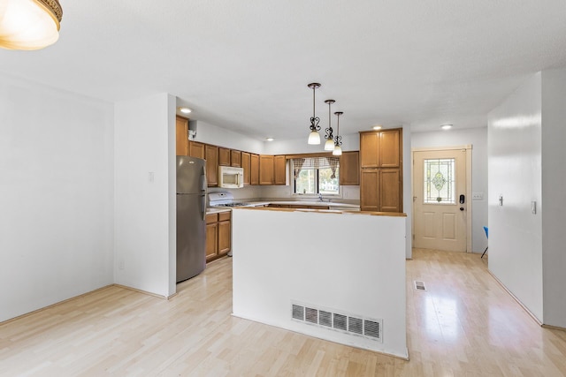 kitchen featuring decorative light fixtures, a center island, white appliances, and light hardwood / wood-style flooring