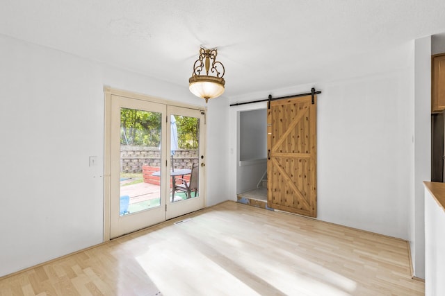 spare room with light wood-type flooring, a barn door, and a textured ceiling