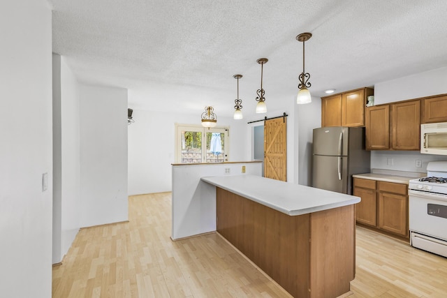 kitchen with a barn door, light hardwood / wood-style floors, white appliances, decorative light fixtures, and a textured ceiling