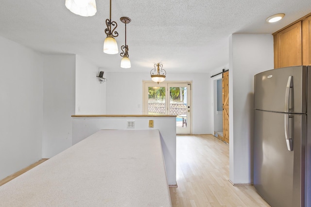 kitchen featuring a textured ceiling, decorative light fixtures, stainless steel refrigerator, light wood-type flooring, and a barn door