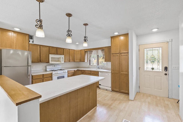 kitchen with hanging light fixtures, sink, white appliances, a textured ceiling, and light hardwood / wood-style floors