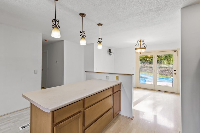 kitchen featuring a textured ceiling, light wood-type flooring, hanging light fixtures, and a center island