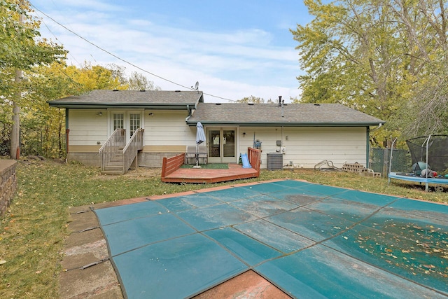 rear view of house with central AC unit, a trampoline, and a covered pool