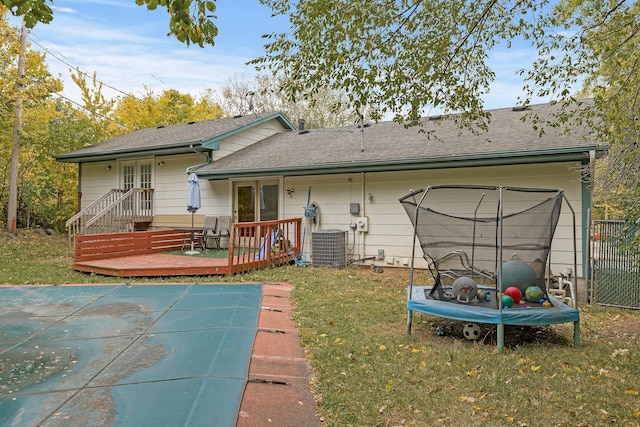 rear view of house with cooling unit, a deck, and a lawn