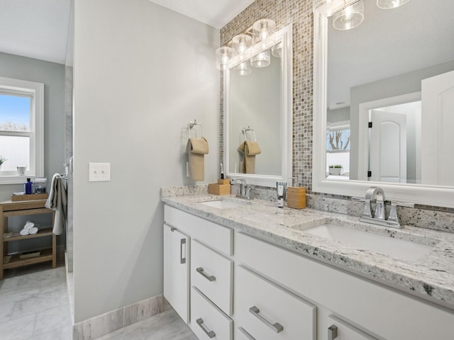 bathroom featuring double vanity, marble finish floor, baseboards, and a sink