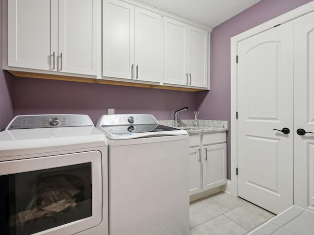 clothes washing area with a sink, washer and dryer, a textured ceiling, cabinet space, and light tile patterned floors