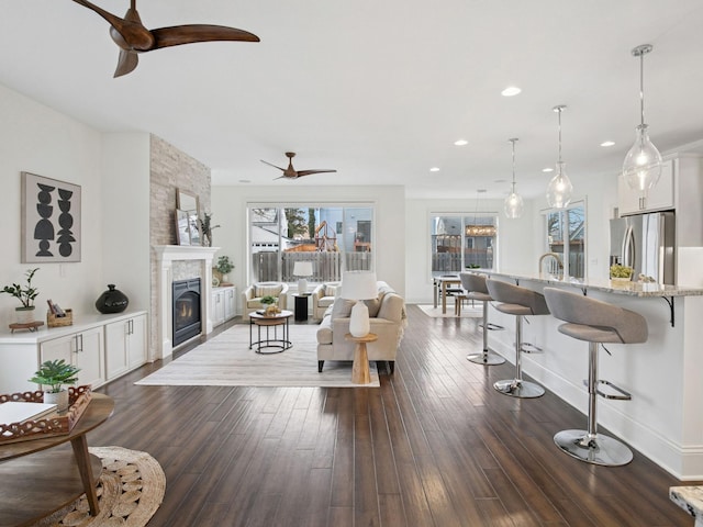 living area with a ceiling fan, recessed lighting, a fireplace, baseboards, and dark wood-style flooring