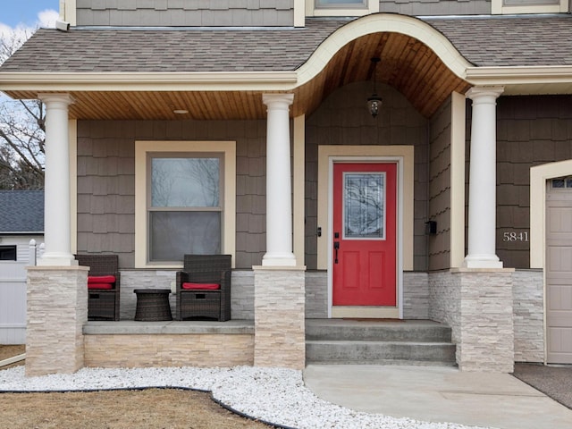 view of exterior entry with covered porch, stone siding, and a shingled roof