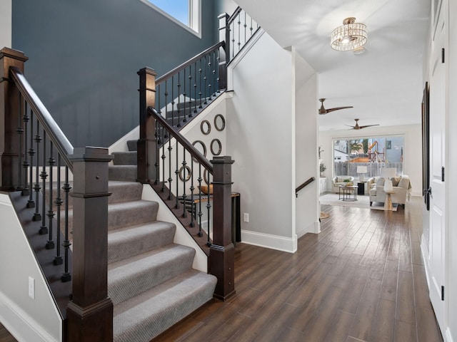 stairs featuring a towering ceiling, ceiling fan with notable chandelier, baseboards, and wood finished floors