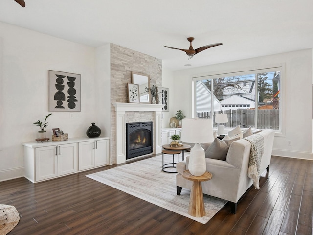 living area featuring baseboards, a fireplace, ceiling fan, and dark wood finished floors