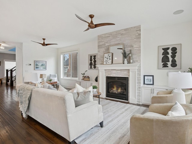 living room featuring a tiled fireplace, dark wood-style floors, stairway, and a ceiling fan