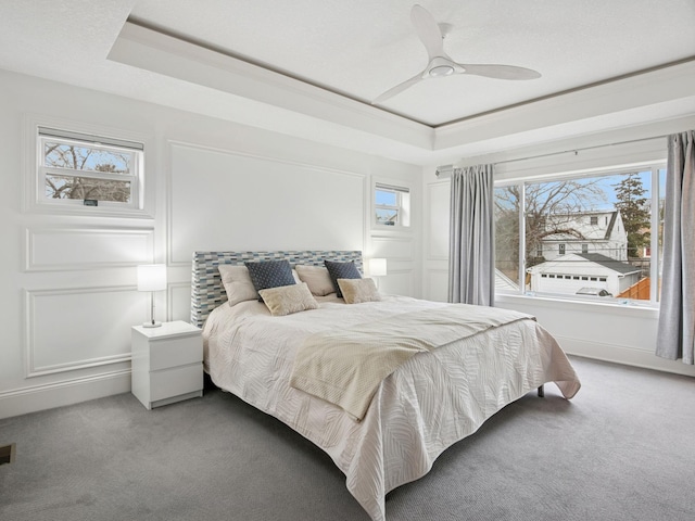 carpeted bedroom with a tray ceiling, a ceiling fan, and a decorative wall