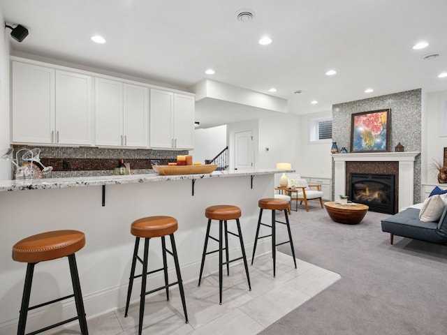 kitchen featuring a glass covered fireplace, a peninsula, light stone countertops, and white cabinetry