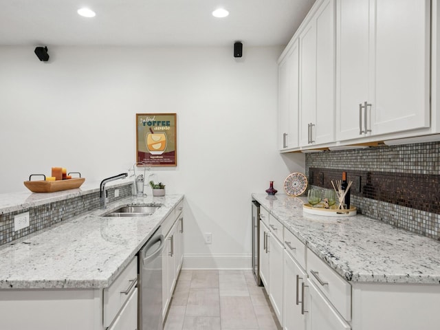 kitchen featuring white cabinetry, a peninsula, a sink, decorative backsplash, and stainless steel dishwasher