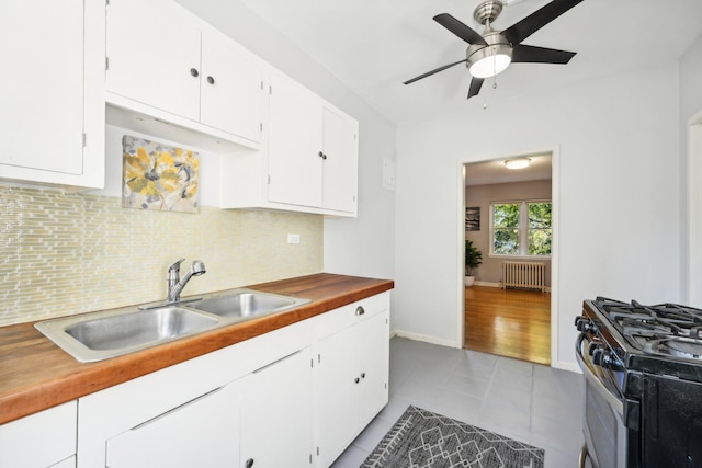 kitchen featuring stainless steel range with gas stovetop, radiator heating unit, sink, and white cabinets