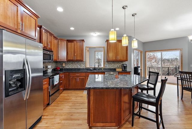 kitchen with decorative light fixtures, a kitchen island, stainless steel appliances, and light hardwood / wood-style flooring