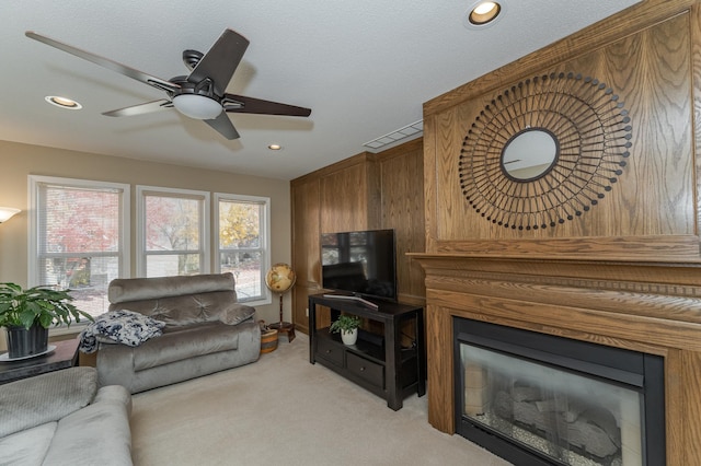 living room with a textured ceiling, light colored carpet, a large fireplace, and ceiling fan