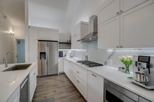 kitchen with wall chimney range hood, sink, white cabinetry, appliances with stainless steel finishes, and light hardwood / wood-style floors