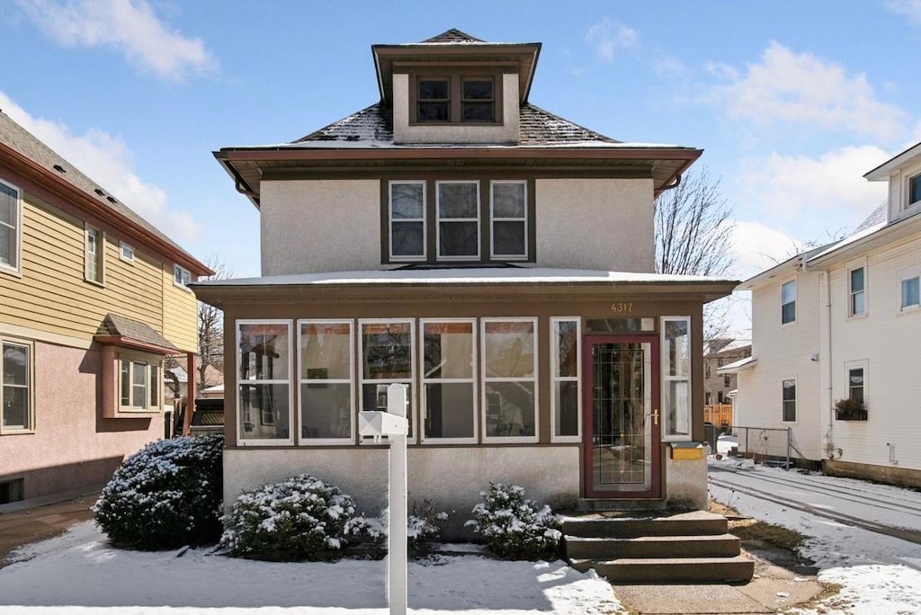 snow covered house with a sunroom and stucco siding