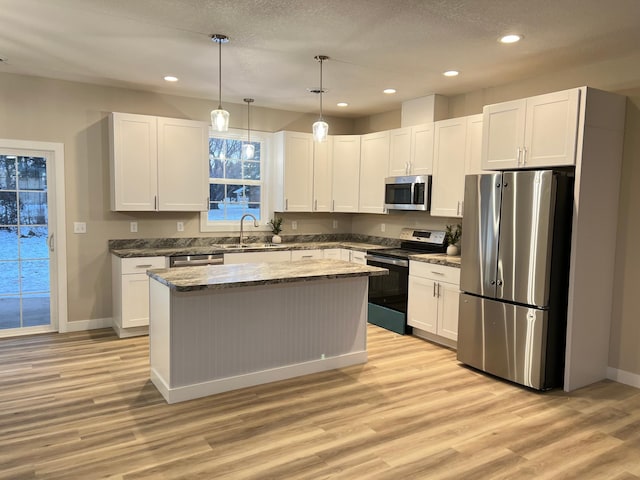 kitchen with sink, white cabinetry, stainless steel appliances, a kitchen island, and decorative light fixtures