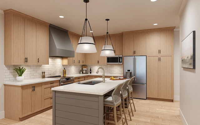 kitchen featuring an island with sink, light wood-type flooring, stainless steel appliances, wall chimney exhaust hood, and sink