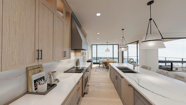 kitchen featuring appliances with stainless steel finishes, sink, hanging light fixtures, light stone counters, and light hardwood / wood-style flooring