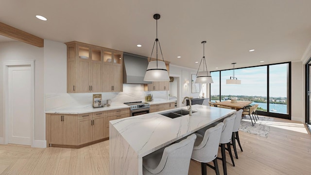 kitchen featuring high end stove, custom range hood, sink, light stone countertops, and a water view