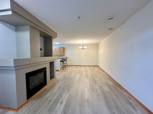 unfurnished living room featuring a chandelier, a textured ceiling, and light wood-type flooring