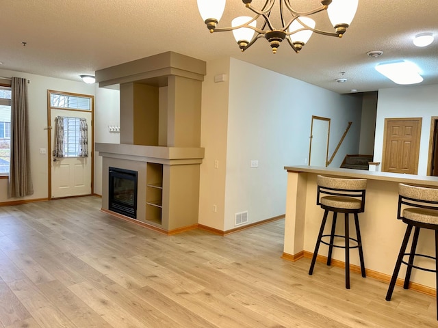 kitchen featuring a kitchen bar, a textured ceiling, decorative light fixtures, light hardwood / wood-style flooring, and a notable chandelier