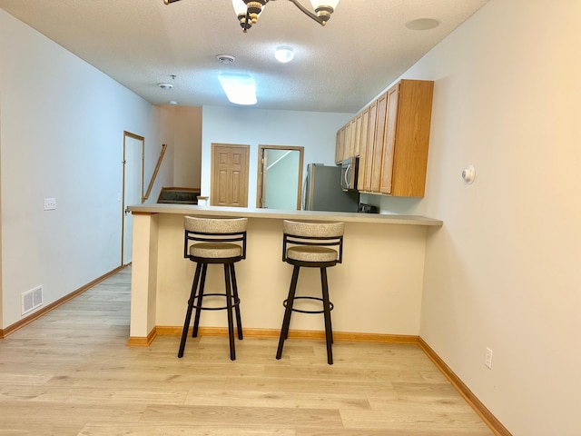 kitchen with a breakfast bar, a textured ceiling, light wood-type flooring, and stainless steel appliances