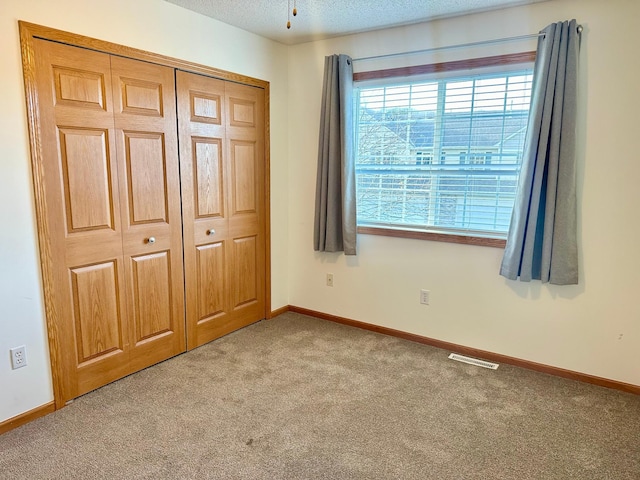 unfurnished bedroom featuring light carpet, a textured ceiling, and a closet