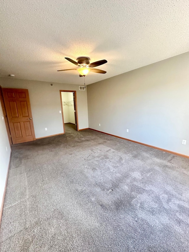 unfurnished bedroom with carpet, a walk in closet, a textured ceiling, ceiling fan, and a closet