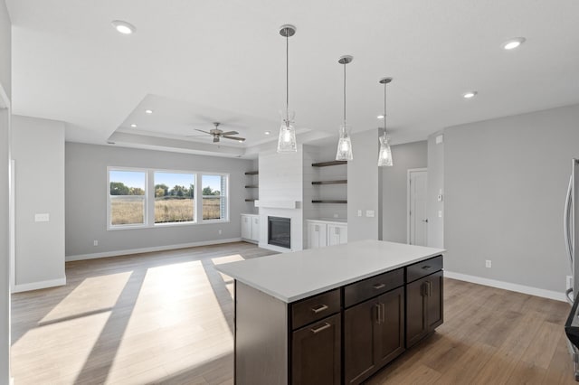 kitchen with a large fireplace, ceiling fan, a kitchen island, pendant lighting, and light hardwood / wood-style floors