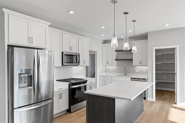 kitchen featuring appliances with stainless steel finishes, sink, a center island, hanging light fixtures, and white cabinets