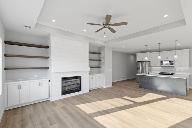 unfurnished living room featuring a large fireplace, a raised ceiling, light hardwood / wood-style floors, and ceiling fan