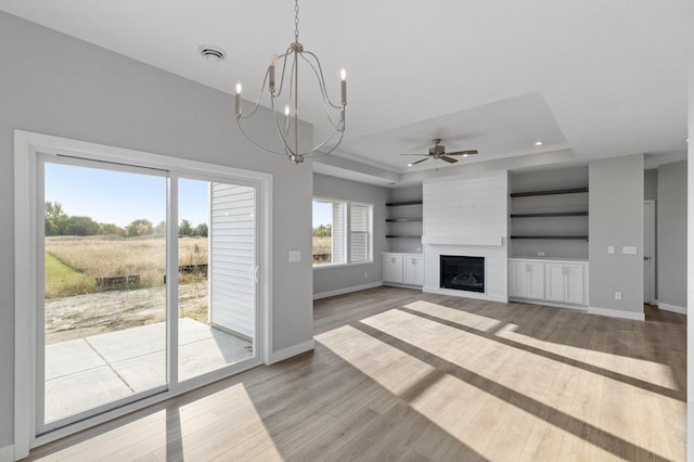 unfurnished living room with wood-type flooring, a tray ceiling, and ceiling fan with notable chandelier