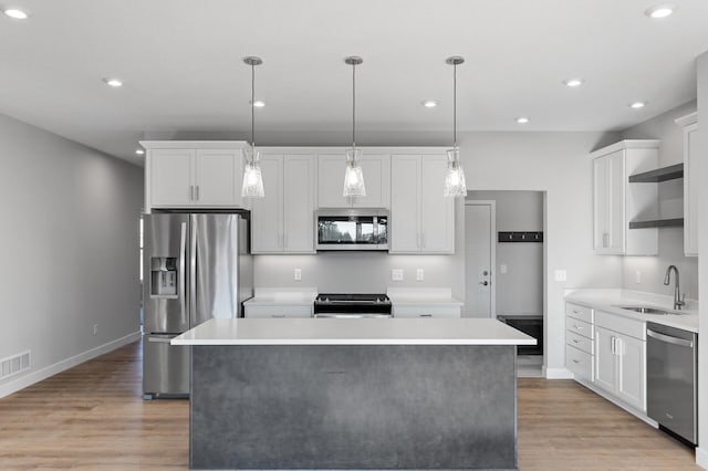 kitchen with appliances with stainless steel finishes, white cabinets, sink, and a kitchen island