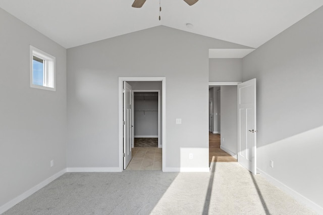 unfurnished bedroom with lofted ceiling, a closet, a spacious closet, light colored carpet, and ceiling fan