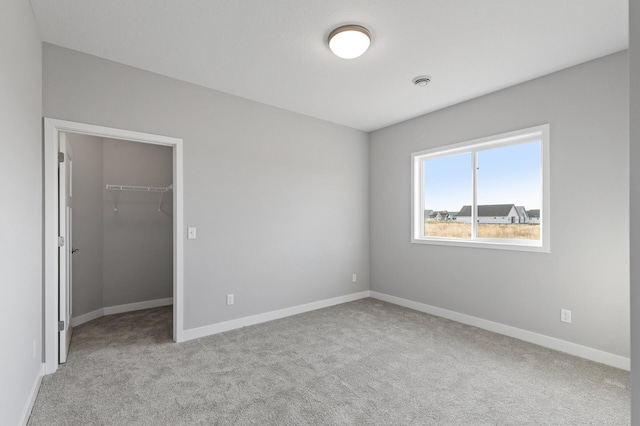 unfurnished bedroom featuring a spacious closet, a closet, and light colored carpet