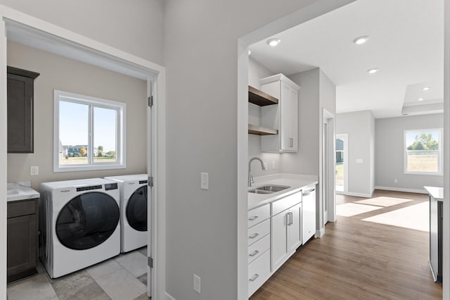 laundry area featuring light hardwood / wood-style floors, sink, washer and clothes dryer, and a wealth of natural light