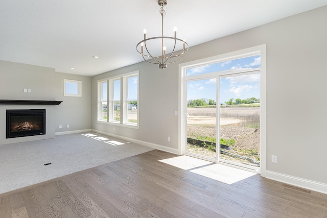 unfurnished living room featuring wood-type flooring, an inviting chandelier, and plenty of natural light