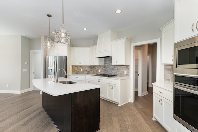 kitchen with appliances with stainless steel finishes, sink, pendant lighting, white cabinetry, and an island with sink