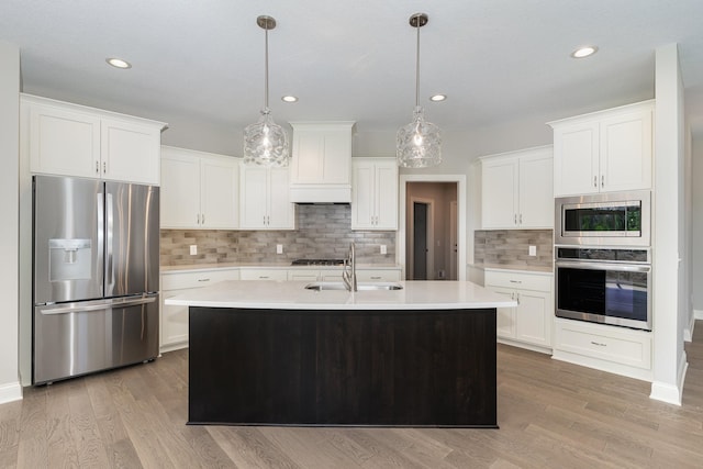 kitchen featuring white cabinets, decorative light fixtures, stainless steel appliances, and a kitchen island with sink