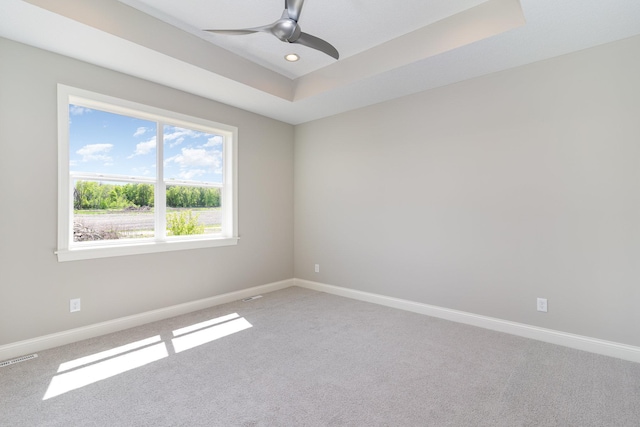 carpeted spare room with ceiling fan and a tray ceiling