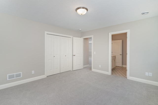 unfurnished bedroom featuring a textured ceiling, connected bathroom, light colored carpet, and a closet