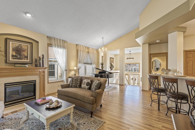 living room with light hardwood / wood-style floors, vaulted ceiling, an inviting chandelier, and a textured ceiling