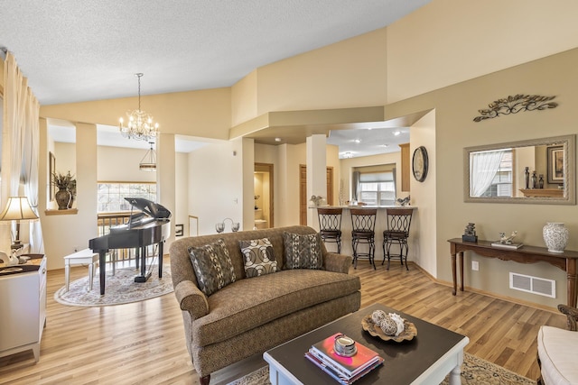 living room featuring light wood-type flooring, a wealth of natural light, a chandelier, and a textured ceiling