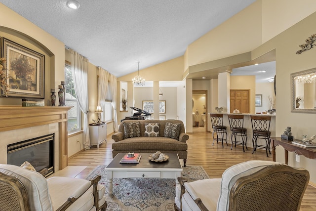 living room featuring a fireplace, light hardwood / wood-style floors, high vaulted ceiling, and a textured ceiling